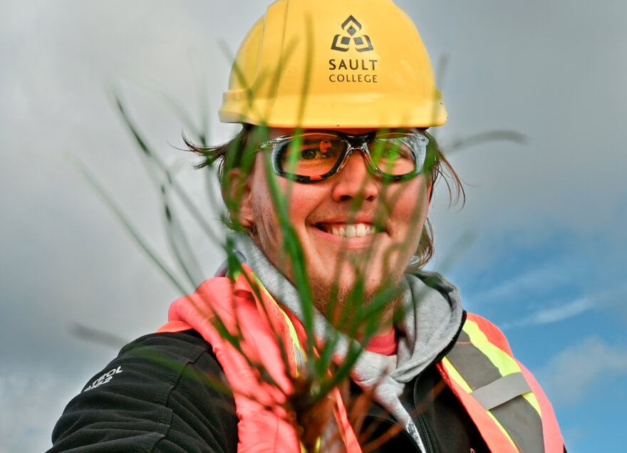 Person with Sault College hard hat holding a plant in front of their face.