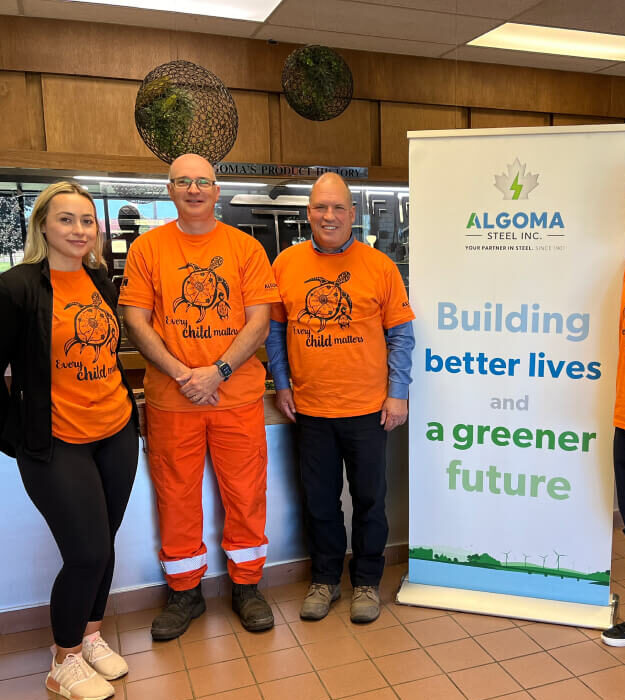 Group of Algoma employees wearing orange "Every Child Matters" t-shorts in front of an Algoma pop-up banner.